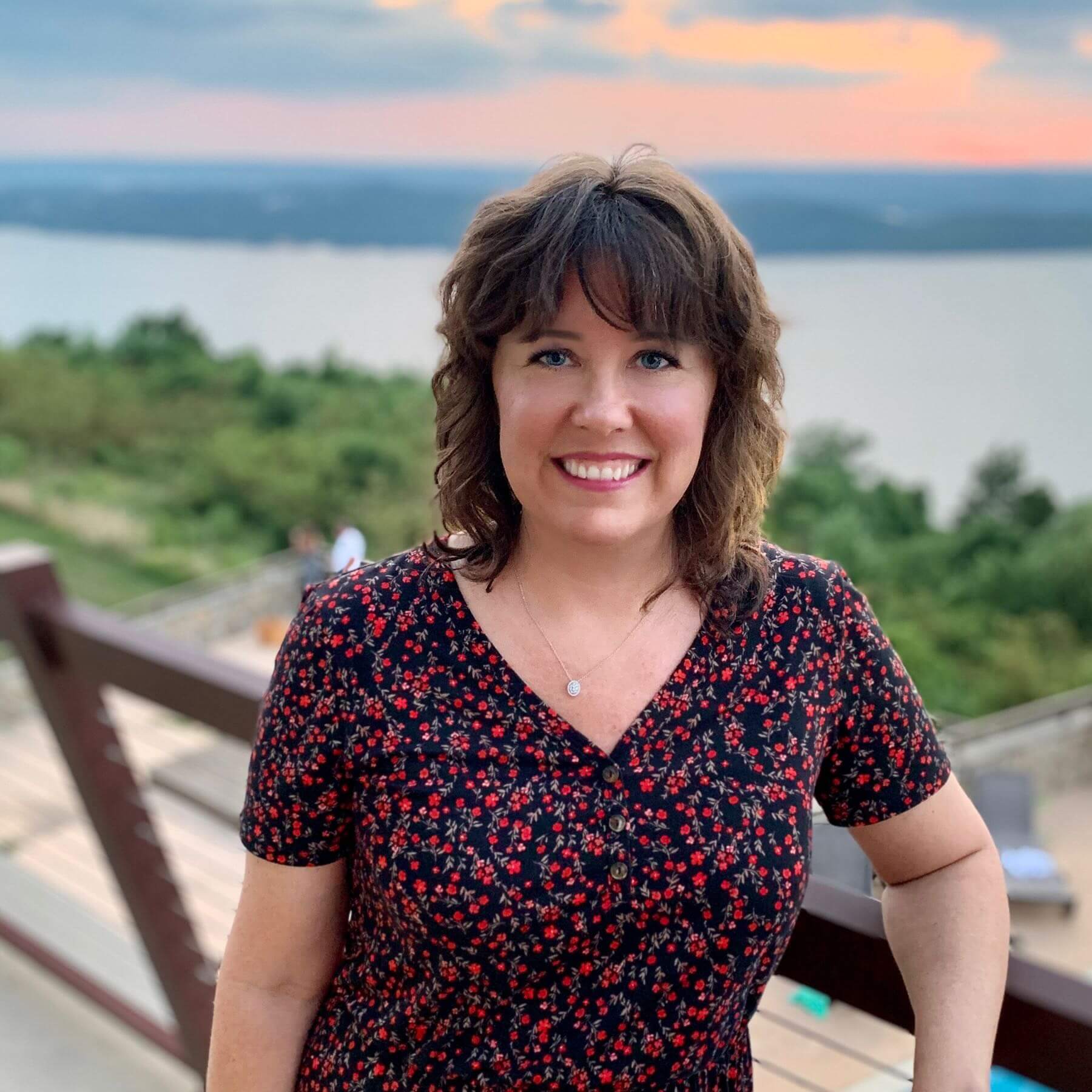 Lindsey Parker smiling at the camera with a sunset and lake in the background.